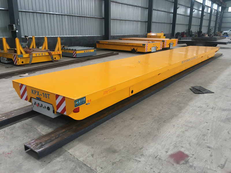 Motorized steel transfer cart on rail for material handling.